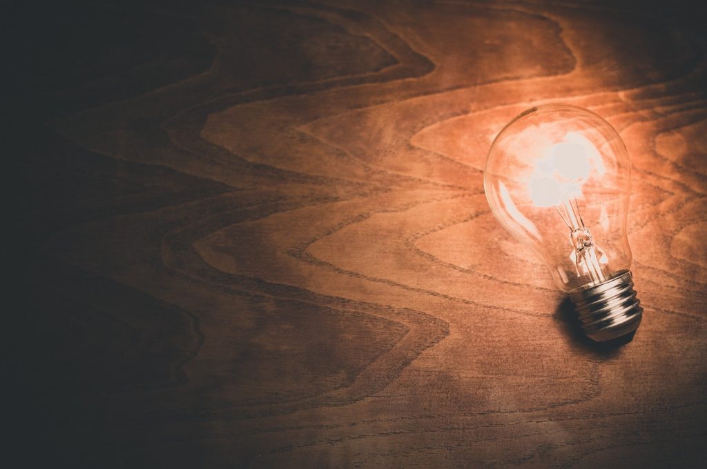 A lit lightbulb casts light on a dark wooden surface