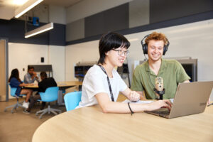 Two students recording a podcast with a mic, laptop and headphones.